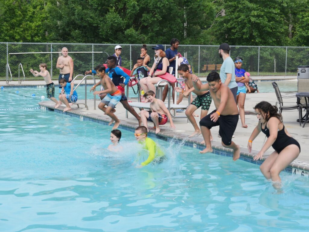 A group of kids all jump into a pool together.